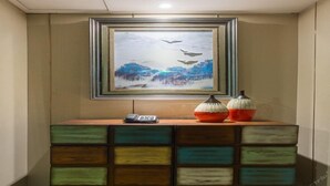 A room with a wooden cabinet with multiple drawers, a framed painting of a snowy landscape, and two decorative pumpkins on top. - Lifeng Tangguo Hotel (Jinhua)