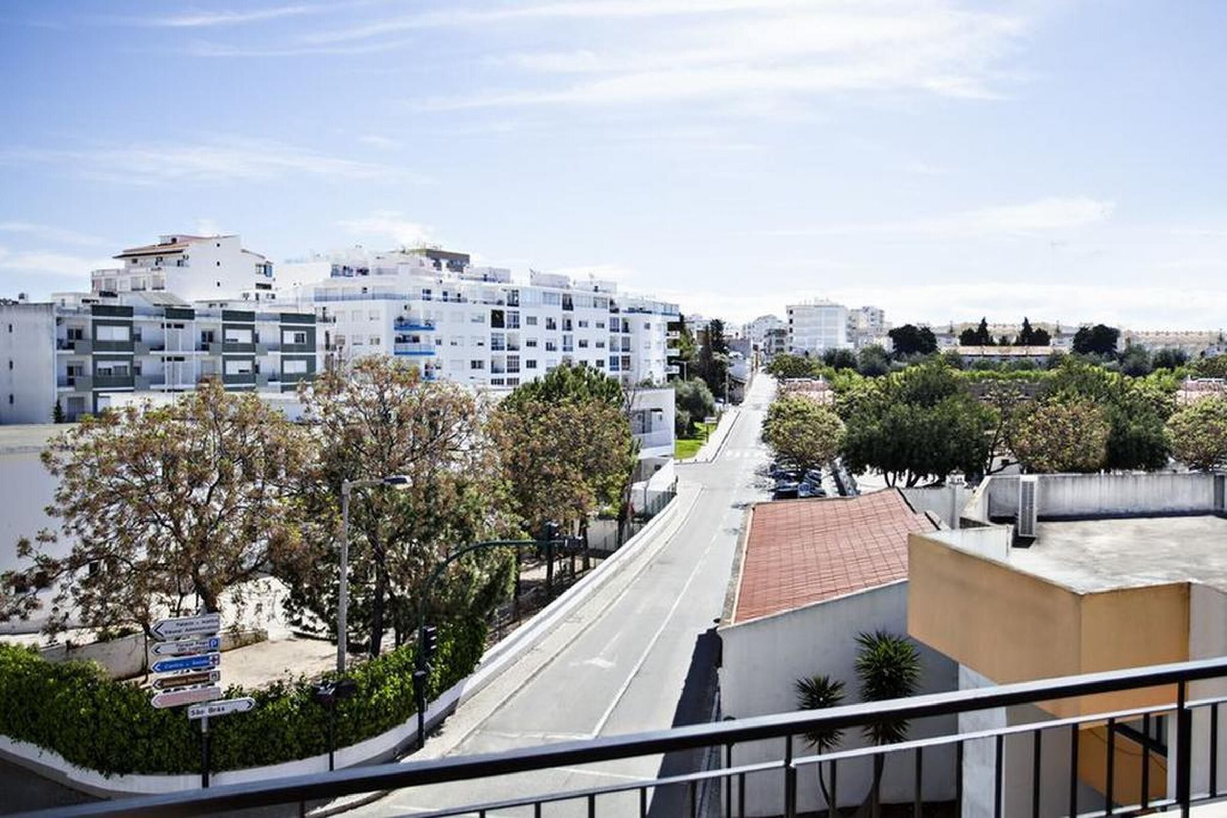 A residential street with modern apartment buildings, a clear sky, and a road with parked cars.