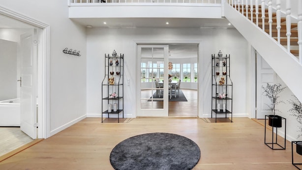 A spacious entryway with a wooden floor, a central rug, and a staircase leading to a balcony. - 6 bedroom cozy home in Grindsted (Grindsted)