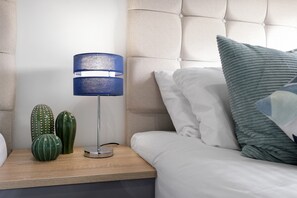 Un dormitorio con cama, mesita de noche, lámpara y cactus decorativos.