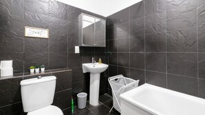 Une salle de bain moderne avec des carreaux de pierre foncée, un lavabo blanc, des toilettes et une baignoire.