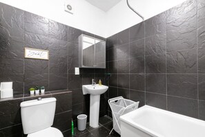 A modern bathroom with dark stone tiles, a white sink, a toilet, and a bathtub.