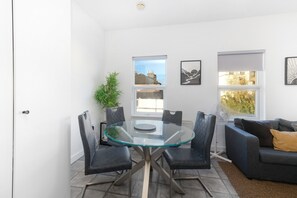 Un salon moderne avec une table à manger à plateau de verre, entourée de chaises, d’un canapé et d’une plante en pot.