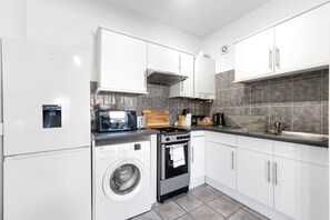 Een moderne keuken met witte kasten, een ingebouwde wasmachine, een fornuis en een magnetron.