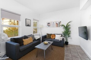 Un salon moderne avec deux canapés, une table basse, un lampadaire et un téléviseur.