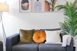 Un sofá gris con tres cojines, una lámpara de pie y una planta verde grande.