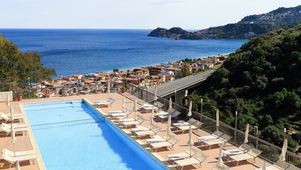 Area piscina con lettini e ombrelloni, con vista su una località costiera e sul mare.