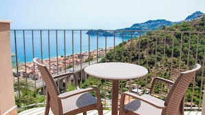 Un balcone con sedie in vimini e un tavolo rotondo, con vista su una cittadina costiera e il mare.