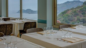 Un restaurant avec des tables dressées pour le service, de grandes fenêtres offrant une vue sur un paysage côtier.