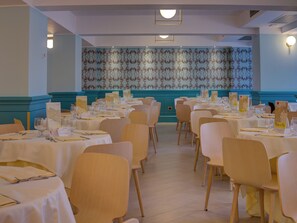 Un espace repas avec plusieurs tables dressées pour un repas, des chaises disposées autour, et un mur décoratif en arrière-plan.