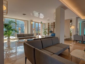 A modern lobby with a large seating area, large windows, and a mix of natural and artificial lighting. - Antares (Letojanni)