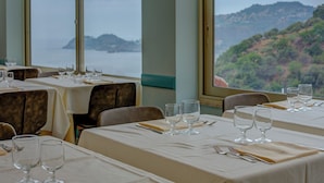Un ristorante con tavoli apparecchiati per la cena, ampie finestre che offrono vista su un paesaggio costiero.