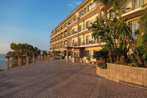 Un hôtel à plusieurs étages, doté de balcons, d’une promenade dallée et offrant une vue sur la mer.