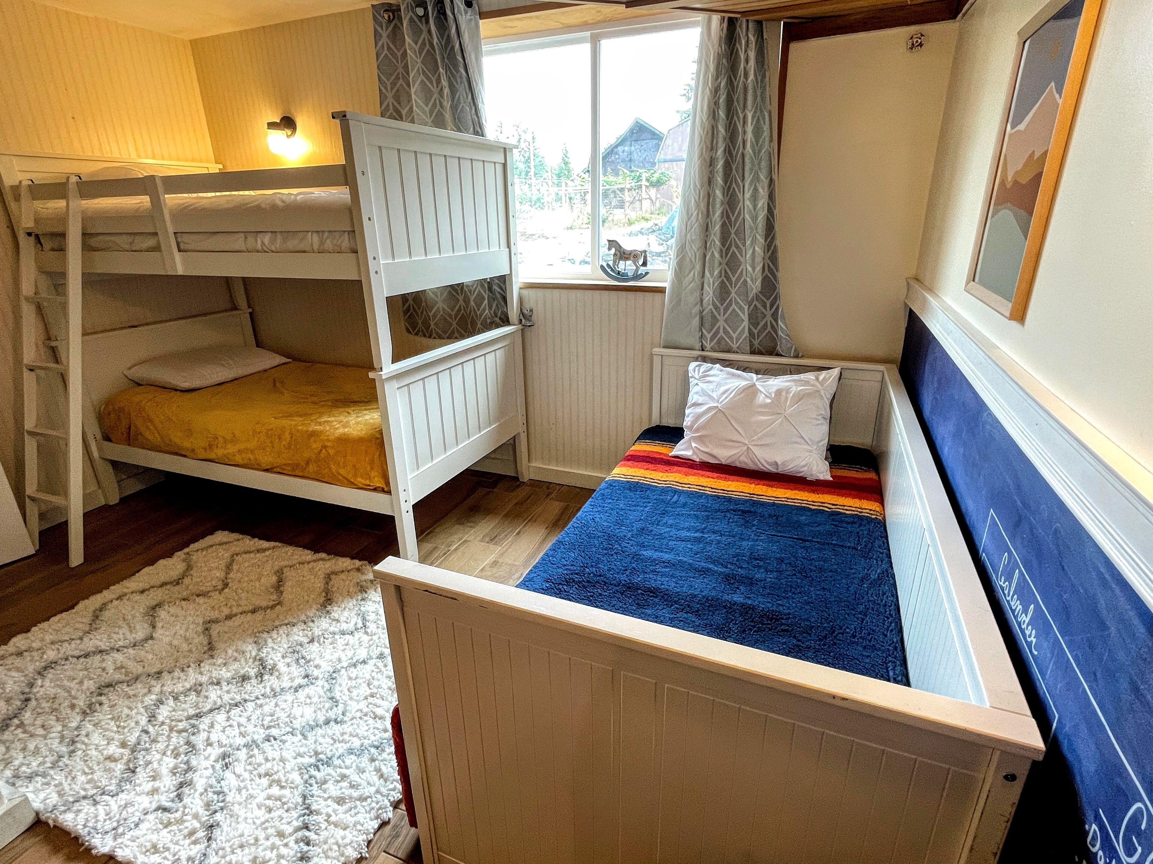 Un dormitorio con una cama litera, una cama individual, una ventana con cortinas, un radiador y una alfombra.