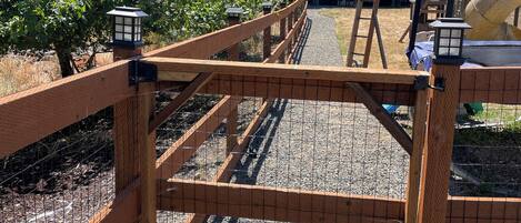 A wooden fence with a gate, gravel ground, and a building with a sloped roof in the background.