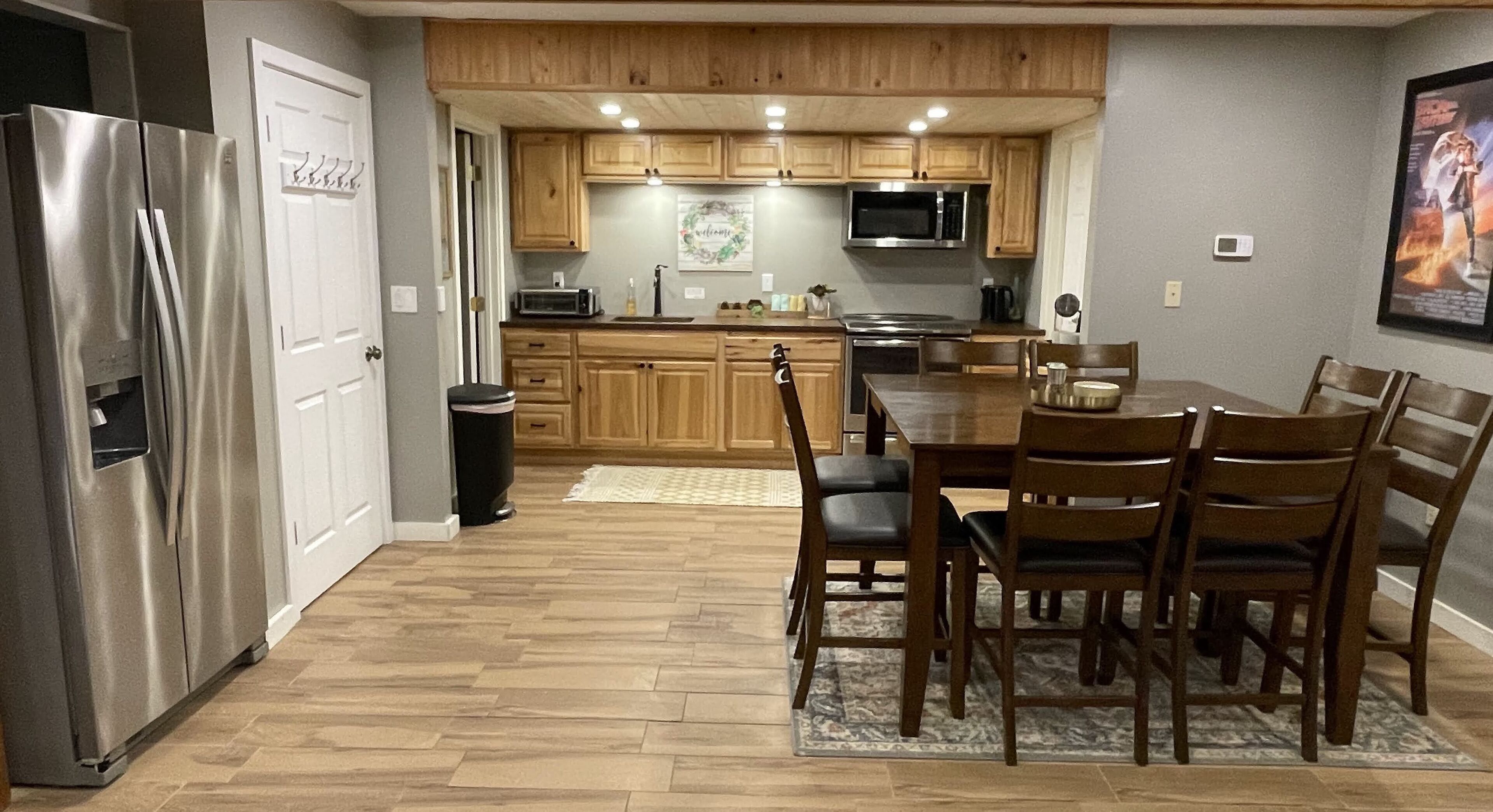 A kitchen with wooden cabinets, a stainless steel refrigerator, a microwave, and a dining area with wooden chairs and a table.