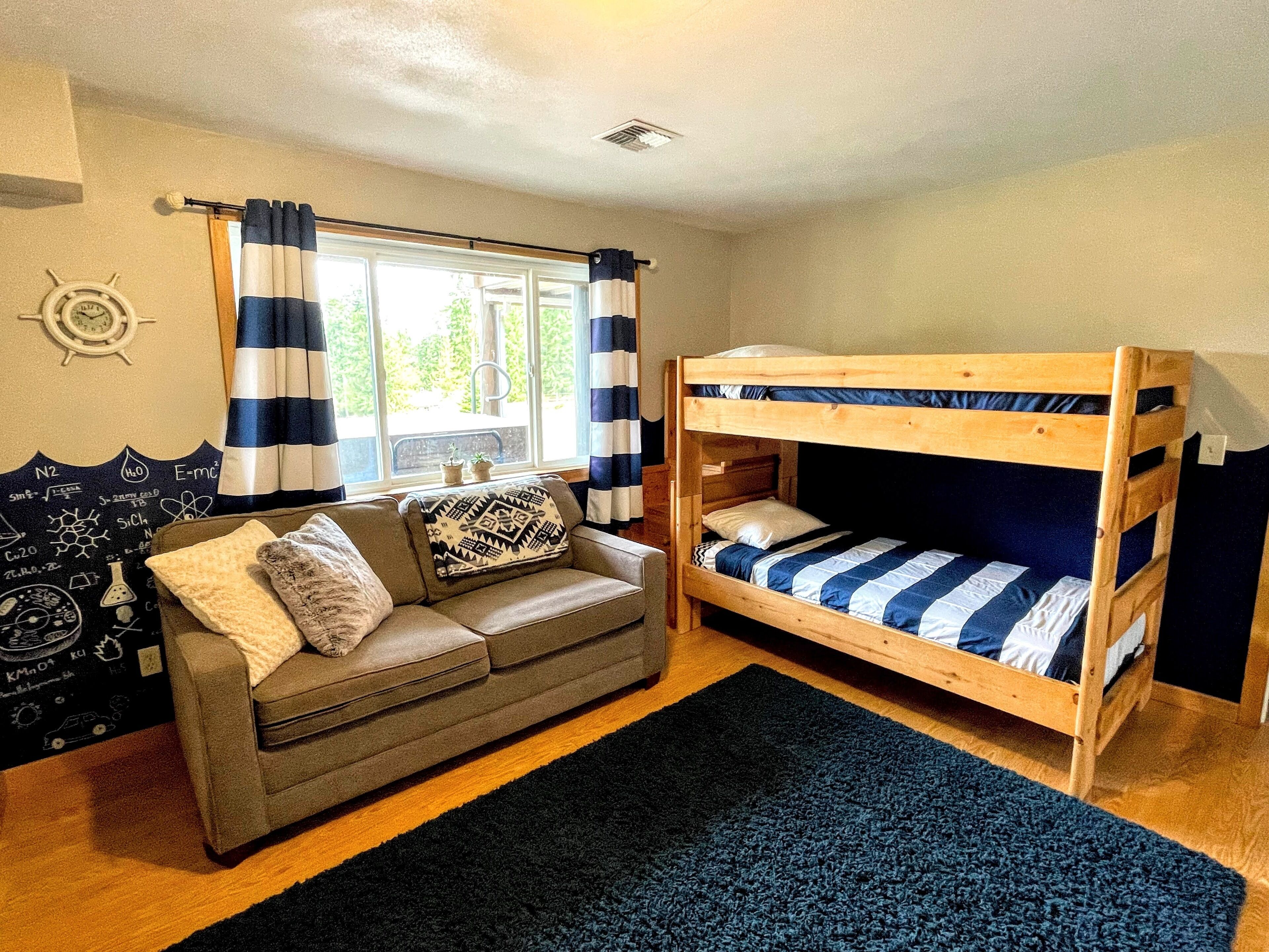 Una habitación con literas, un sofá, una ventana con cortinas y un reloj de pared.