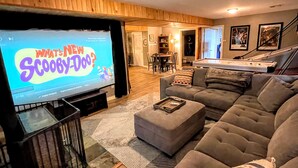 A living room with a television displaying 'What's New Scooby-Doo?', a grey sofa, a coffee table, and a pool table in the background.