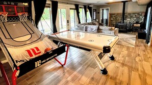 A pool table in a room with a basketball hoop, a stone fireplace, and a view of the outdoors.