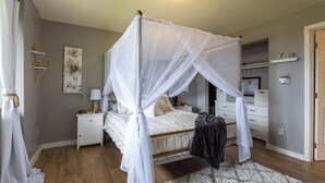 A bedroom with a four-poster canopy bed, a nightstand, a dresser, and a closet.