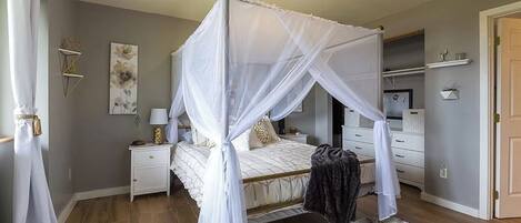 A bedroom with a four-poster canopy bed, a nightstand, a dresser, and a closet.
