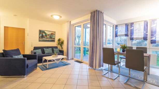 Een woonkamer met een bank, salontafel en een zithoek met stoelen en een tafel.