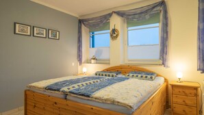 Een slaapkamer met een houten bed, twee nachtkastjes, een raam met gordijnen en drie ingelijste foto's aan de muur.