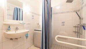 Een badkamer met een wastafel, spiegel, douche en een handgreep.