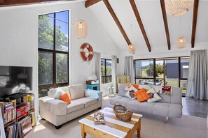 Un salón espacioso con dos sofás, una mesa de centro y una estantería. Amplios ventanales ofrecen abundante luz natural y vistas al exterior.