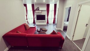 A living room with a red sofa, a coffee table, and a flat-screen TV mounted on the wall. - Kent Suites Hotels (Istanbul)