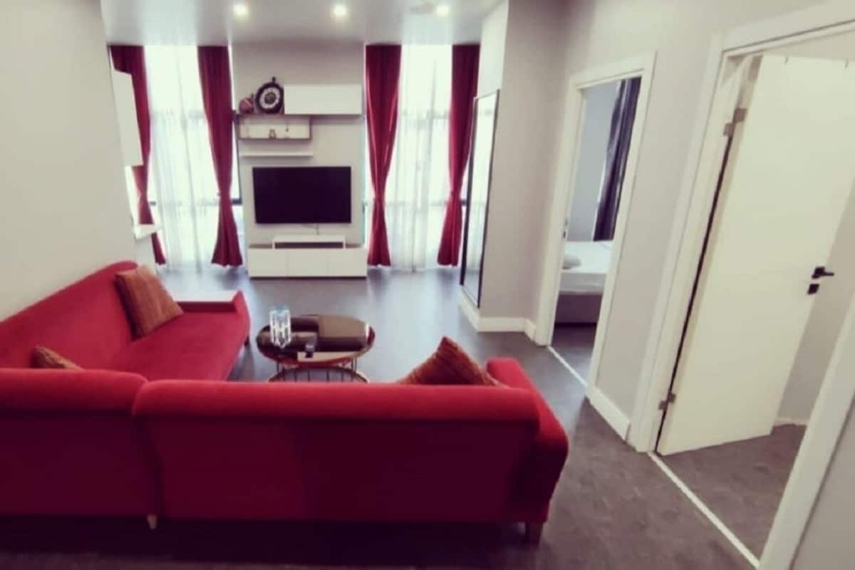 A living room with a red sofa, a coffee table, and a flat-screen TV mounted on the wall.