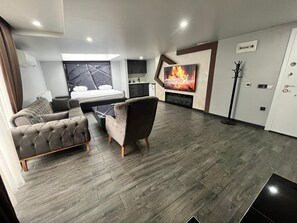 A modern living room with a sofa, armchair, and a flat-screen TV mounted on the wall. - Kent Suites Hotels (Istanbul)