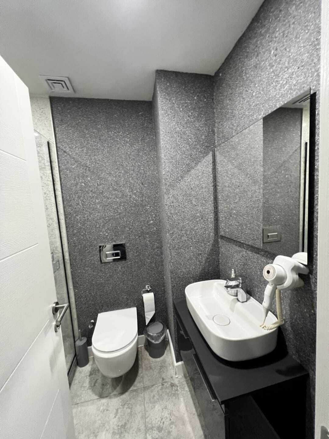 Une petite salle de bain avec des toilettes blanches, un lavabo avec un miroir et un sèche-cheveux.