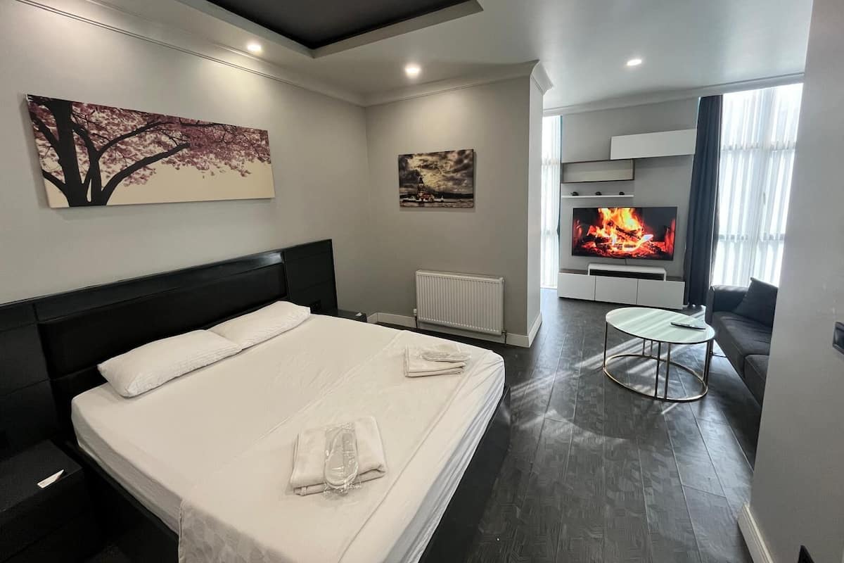 A modern hotel room with a large bed, a TV, a fireplace, and a dining area.