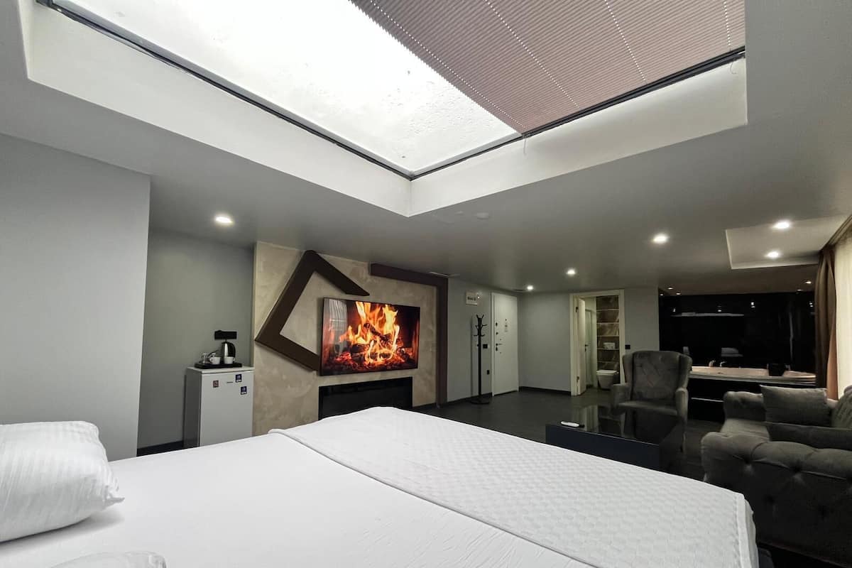 A modern hotel room with a skylight, a bed, a seating area, and a fireplace.