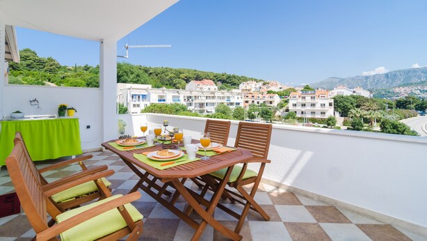 A balcony with a table set for breakfast, overlooking a hillside of buildings. - Apartment Jossy (Dubrovnik)