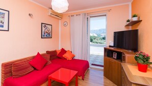 A modern living room with a sofa, a small table, a TV, and a balcony with a view. - Apartment Jossy (Dubrovnik)