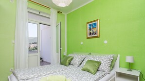 A room with a bed, a nightstand, a lamp, a painting, and a view through a door. - Apartment Jossy (Dubrovnik)