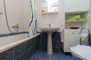 Ein Badezimmer mit einer Badewanne, einem Standwaschbecken, einer Toilette und einem Ablagefach für Toilettenartikel.