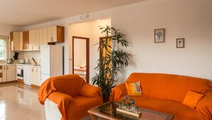 Ett vardagsrum med en orange soffa och fåtölj, ett soffbord, en krukväxt och ett kök i bakgrunden.