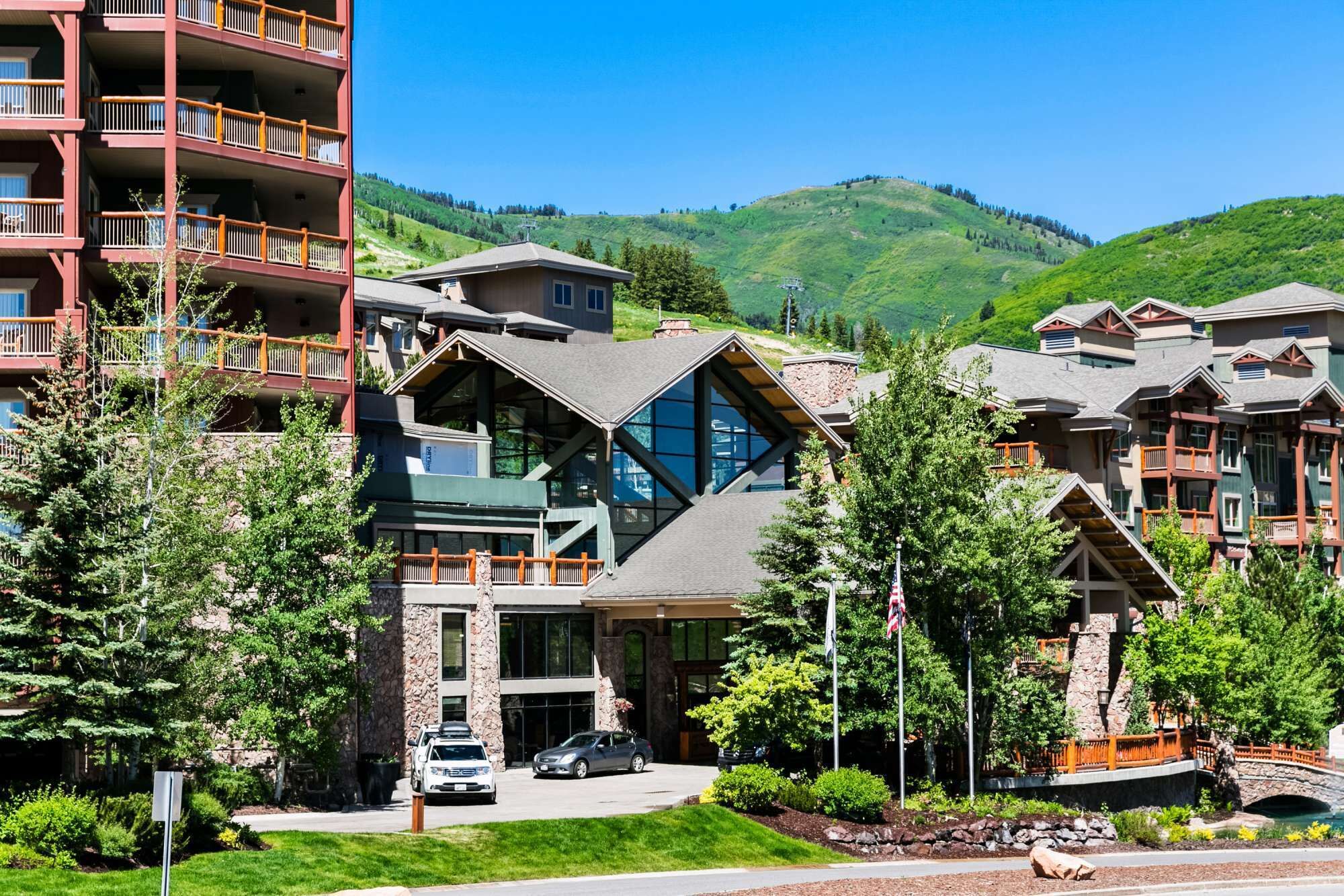 A modern hotel with a prominent glass facade, multiple balconies, and a view of a mountainous landscape.