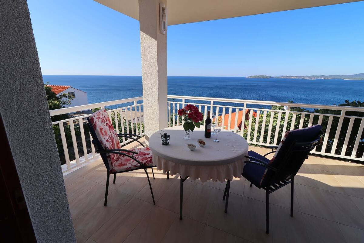 Un balcón con mesa, sillas y vista al mar.