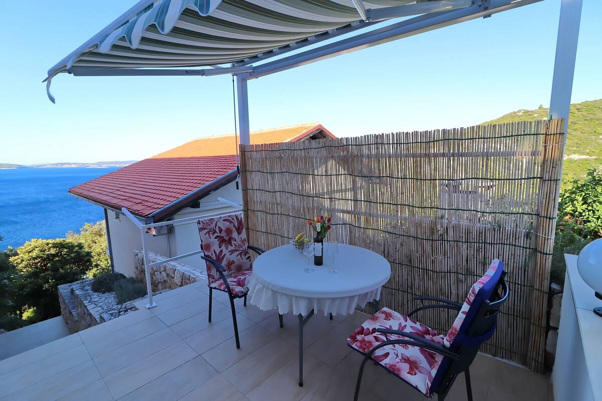 Un patio techado con una mesa redonda y sillas, vista al mar y cerca de bambú.