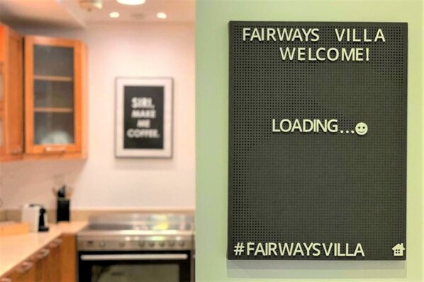 A kitchen with wooden cabinets, a stainless steel oven, and a framed sign on the wall. - Fairways Villa at Al Hamra Village (Ras Al Khaimah)