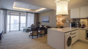 Ein Hotelzimmer mit einer großen Schiebeglasdoor zum Balkon, einer Sitzecke mit einer Couch und Sesseln, einer Waschmaschine und einer Küchenzeile.