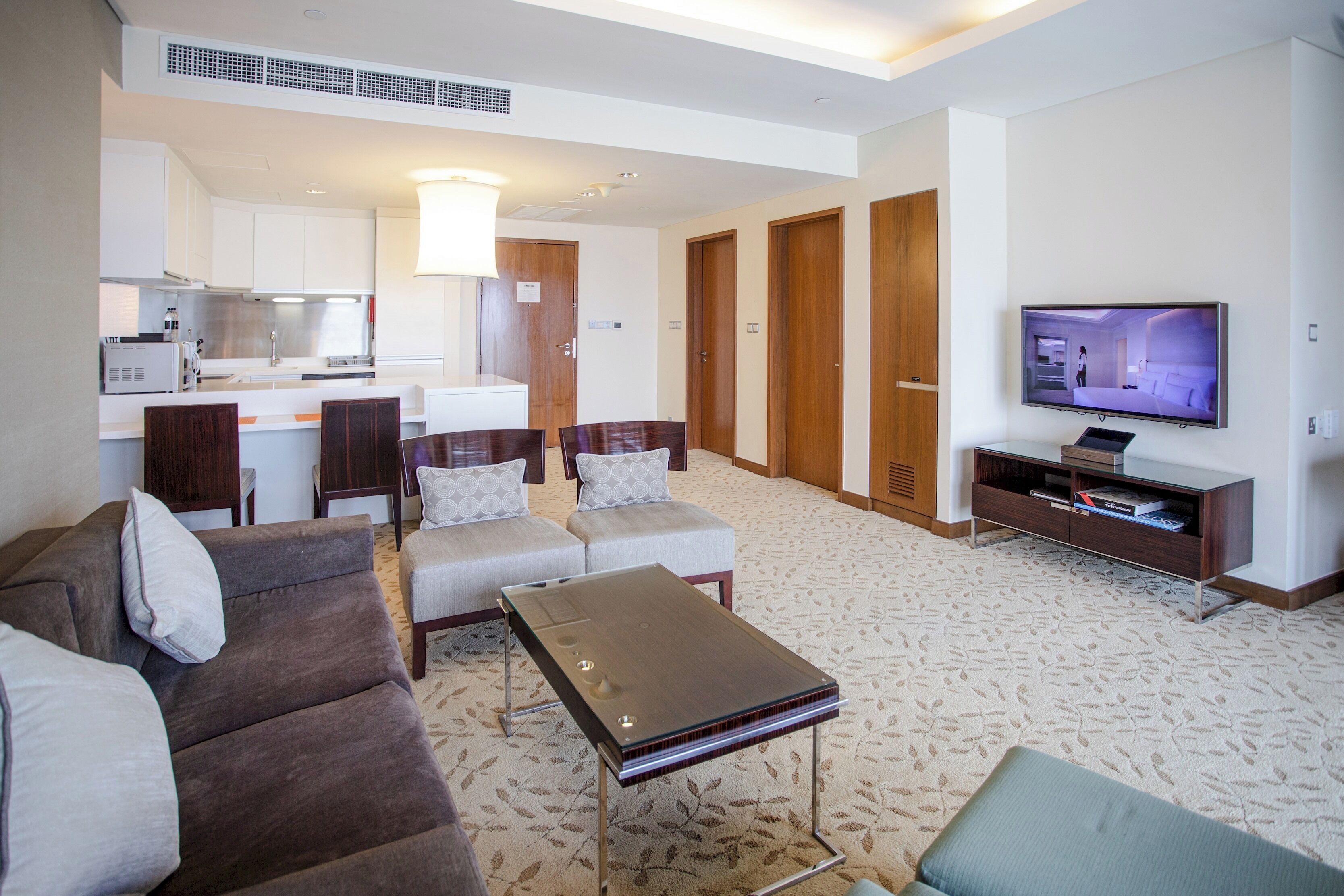 A modern hotel room with a living area, kitchenette, and a TV displaying a bedroom.