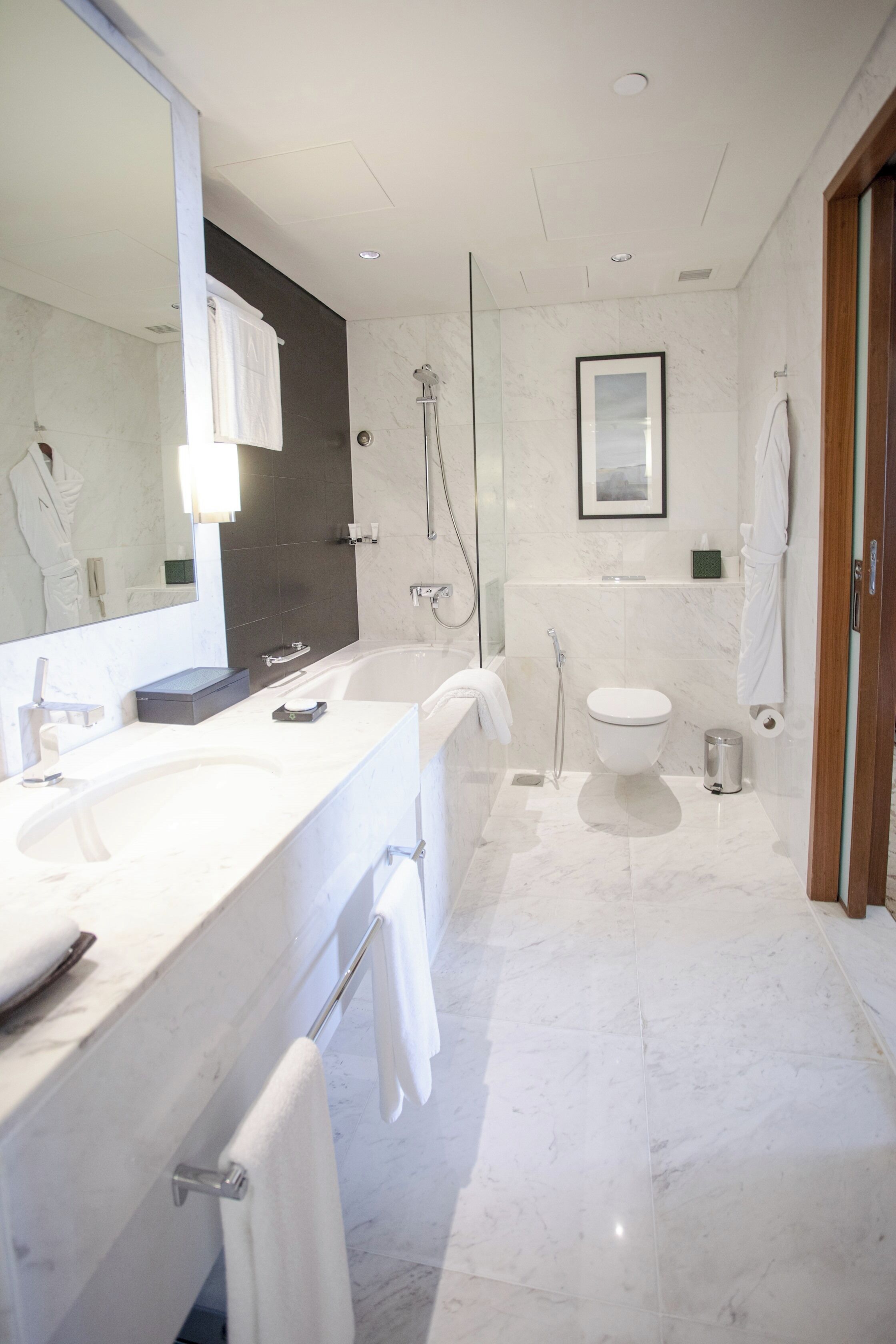 A modern bathroom with a large mirror, dual sinks, a bathtub, and a toilet.