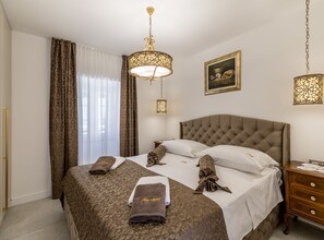 A hotel room with a large bed, two bedside tables, a nightstand, a painting on the wall, and a chandelier. - Holiday Home Granny Mary (Sutivan)