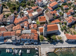 An aerial view of a coastal town with terracotta-roofed buildings, a marina with boats, and a prominent church. - Holiday Home Granny Mary (Sutivan)