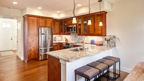A modern kitchen with wooden cabinets, stainless steel appliances, a marble countertop, and pendant lighting.